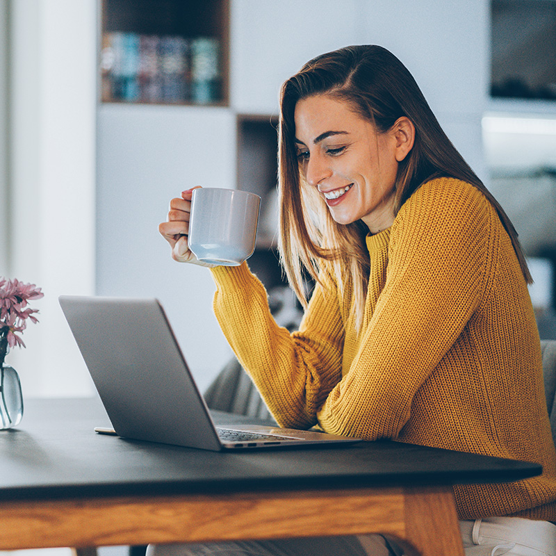 a woman reviewing finances info at home on a laptop while enjoying coffee