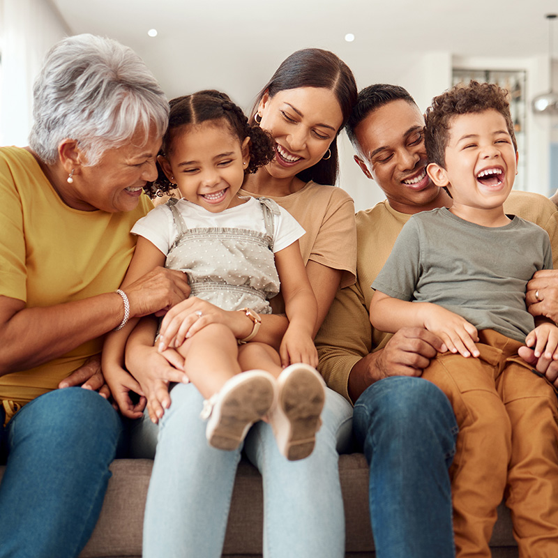 three generations of a family laughing while sitting on a couch