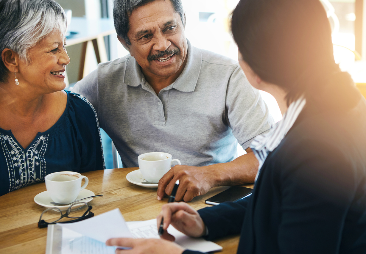 a senior couple in discussion with a financial advisor over coffee